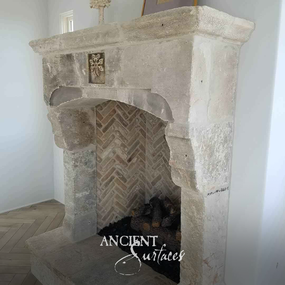 Rustic weathered limestone fireplace mantel with a small carved rosette panel, shaped corbel lintel and herringbone brick firebox