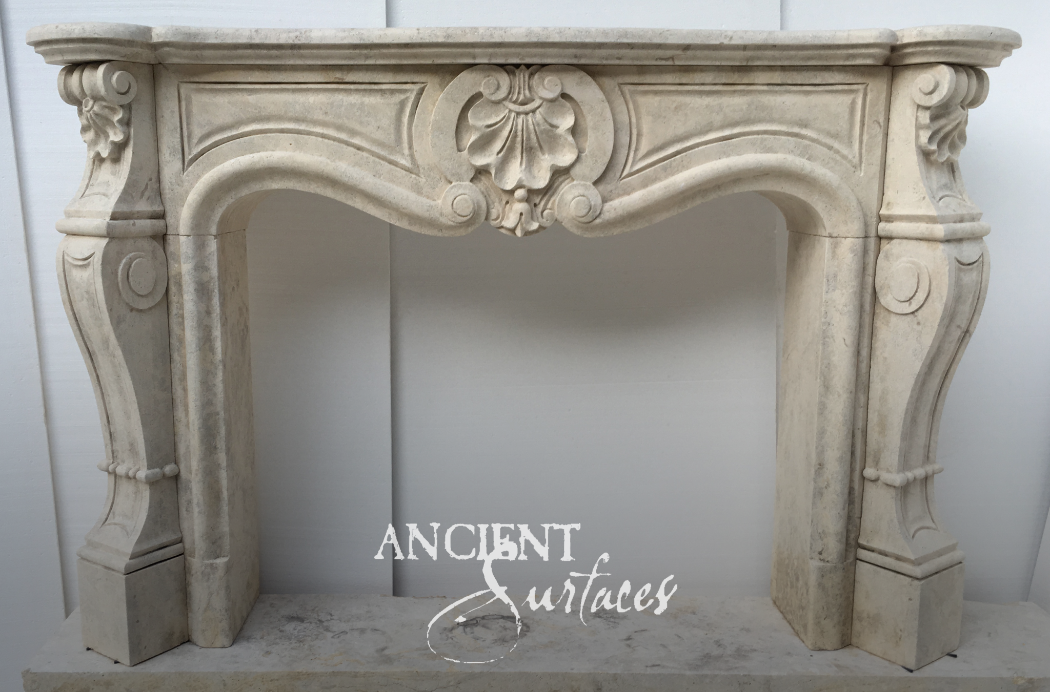 Reclaimed limestone fireplace mantel by Ancient Surfaces with a carved scallop shell cartouche, serpentine arched opening and scrolled acanthus console jambs