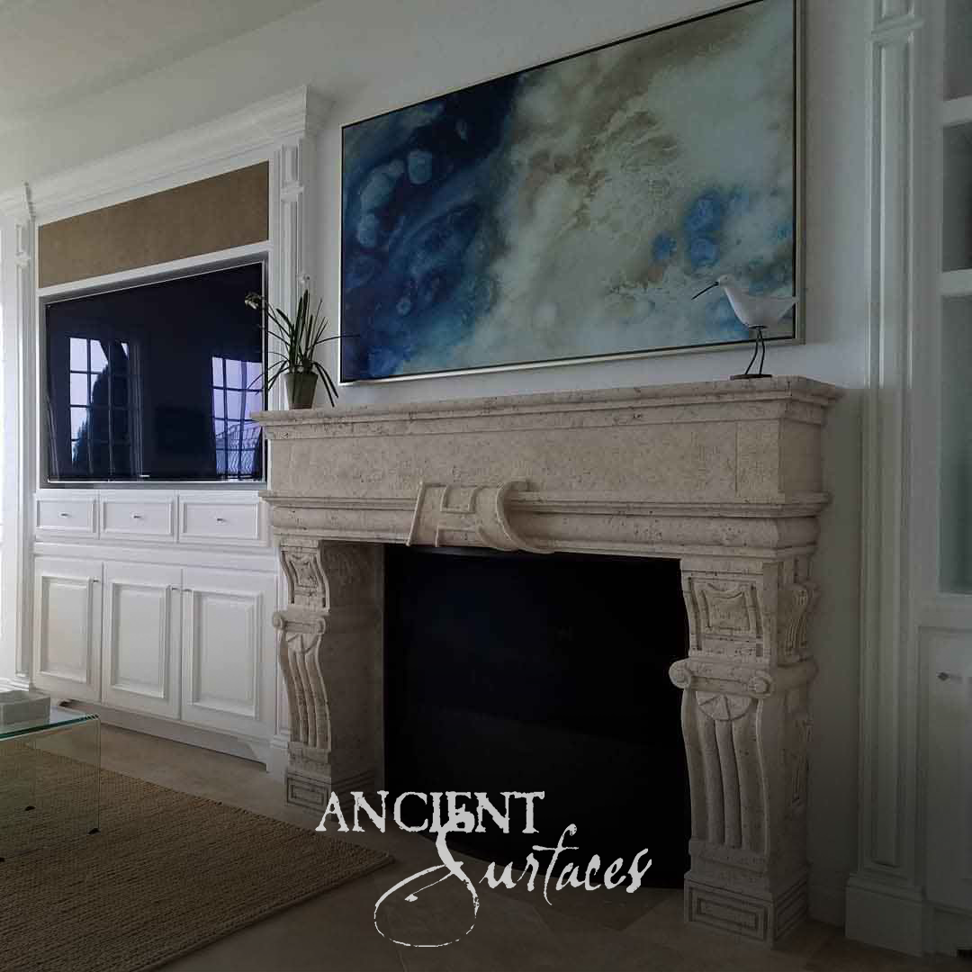 Pale reclaimed limestone fireplace mantel with a carved scrolled keystone and stacked fluted console jambs in a bright living room
