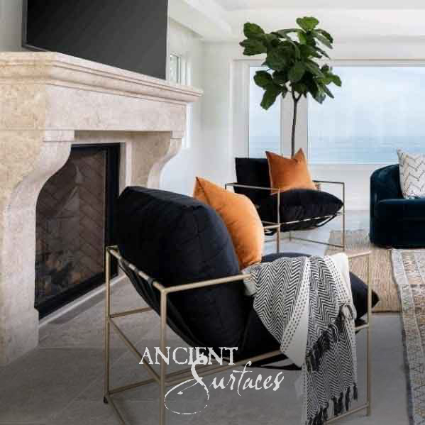 Pale smooth limestone fireplace mantel with a deep molded cornice and curved corbels around a herringbone firebox in a bright seaside living room