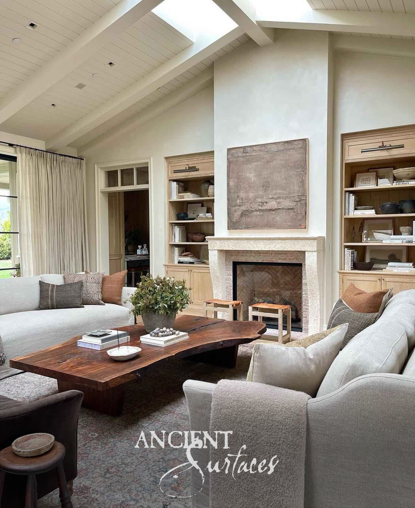 Slender pale limestone fireplace surround with a narrow molded shelf framing a herringbone brick firebox beneath a vaulted ceiling